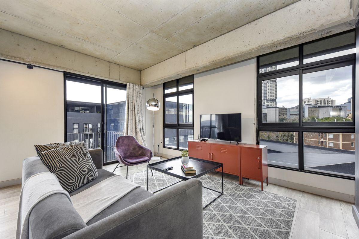 Modern living room featuring an industrial-style exposed concrete ceiling, large black-framed windows, and access to a balcony with urban views.
