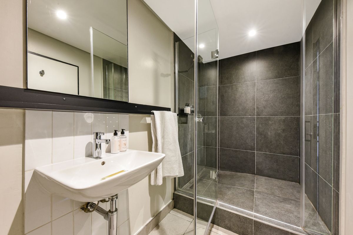 Modern bathroom featuring a walk-in shower with dark tiling, a wall-mounted basin with chrome fixtures, and recessed lighting.