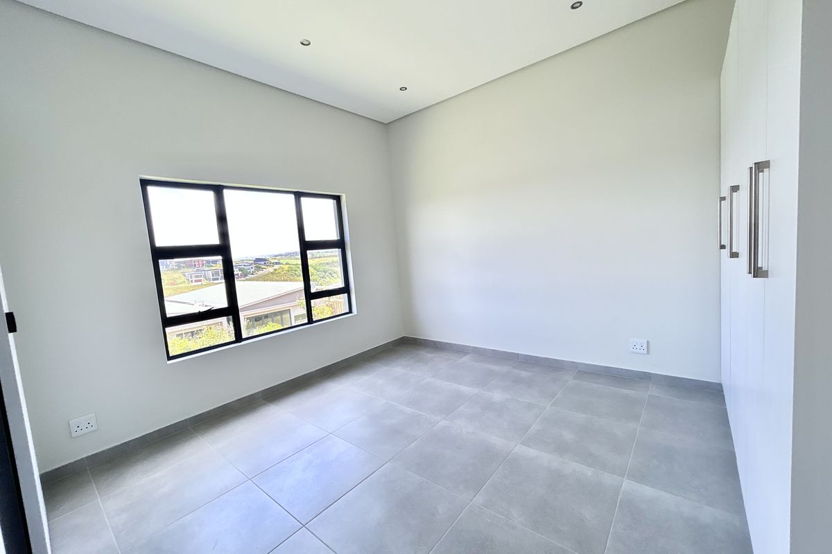 A bright, modern, and empty bedroom featuring neutral tiled flooring, built-in cupboards, and large windows with scenic views.