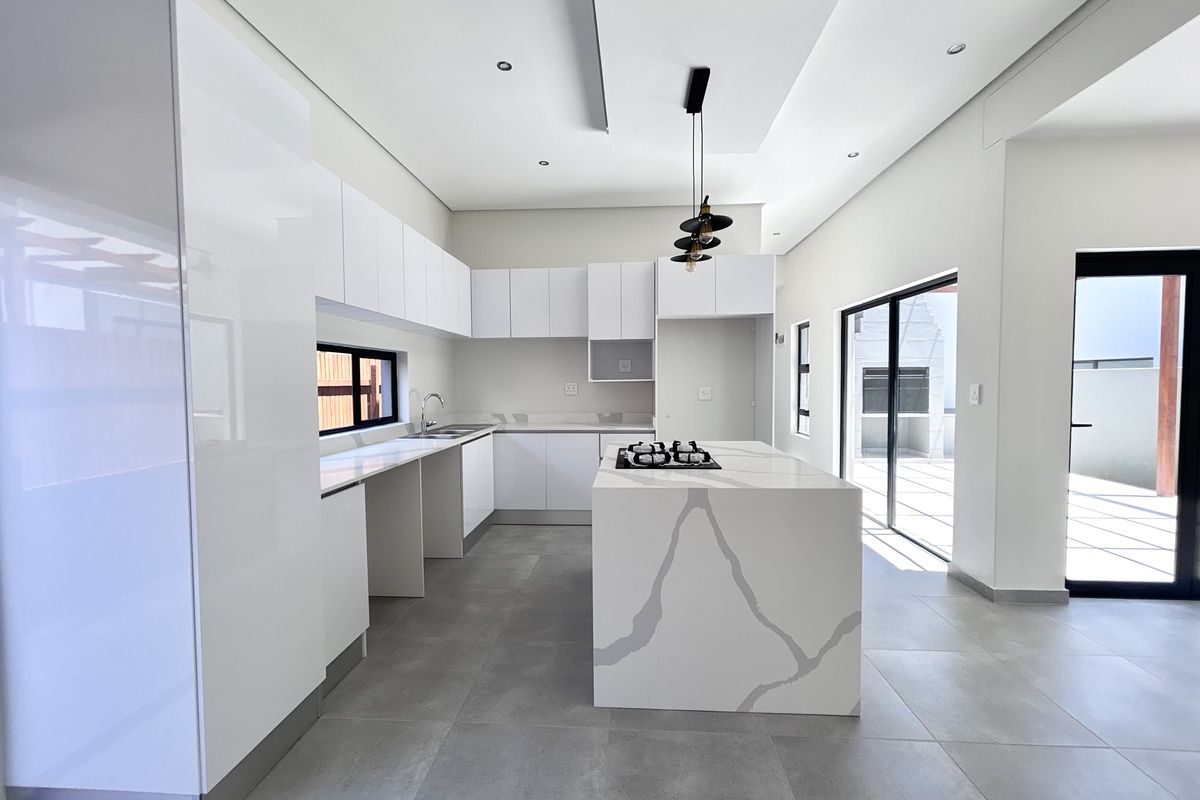 Modern, minimalist kitchen featuring a large stone-topped island with a built-in hob, sleek white cabinetry, and large sliding doors leading to the patio.