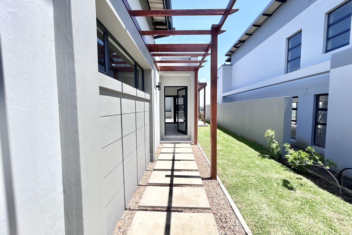 A modern side passage featuring a timber pergola, concrete paver walkway, and well-maintained lawn area leading to a glass entrance door.
