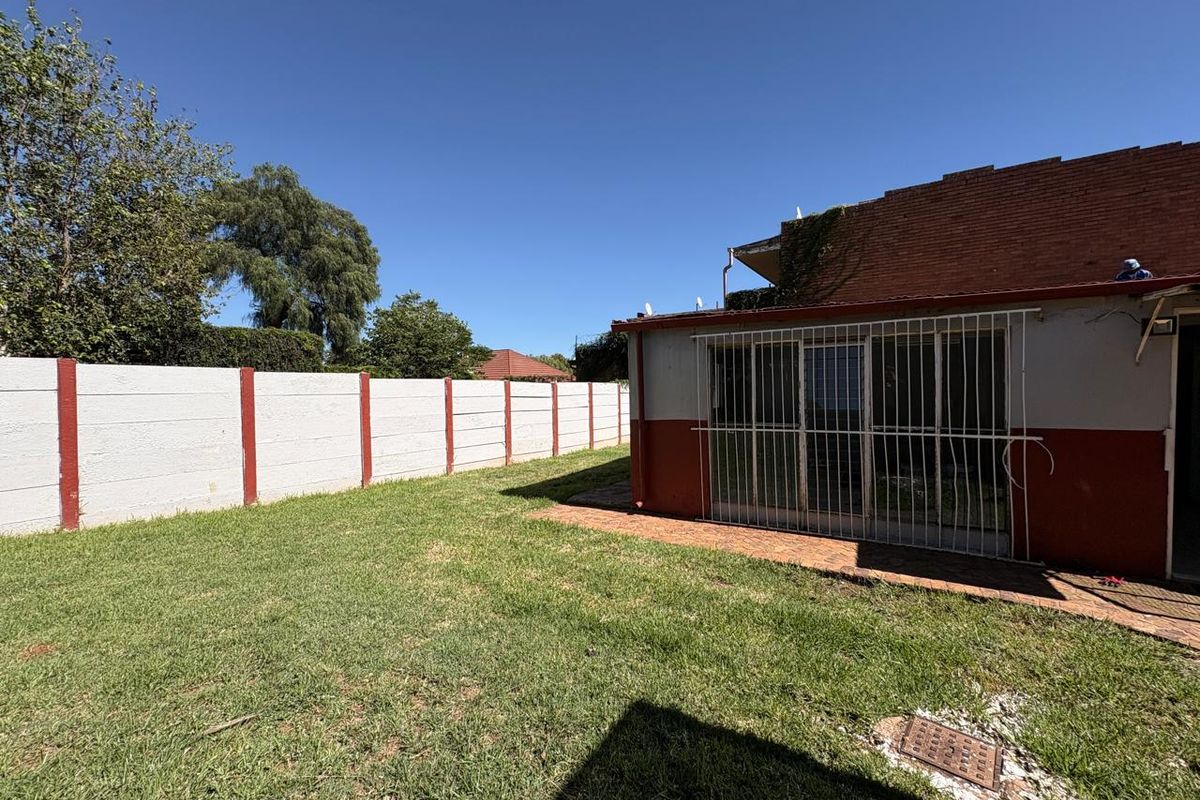 Rear exterior view of the property featuring a lawn, brick paved area, and a precast concrete boundary wall with security bars on the sliding door.