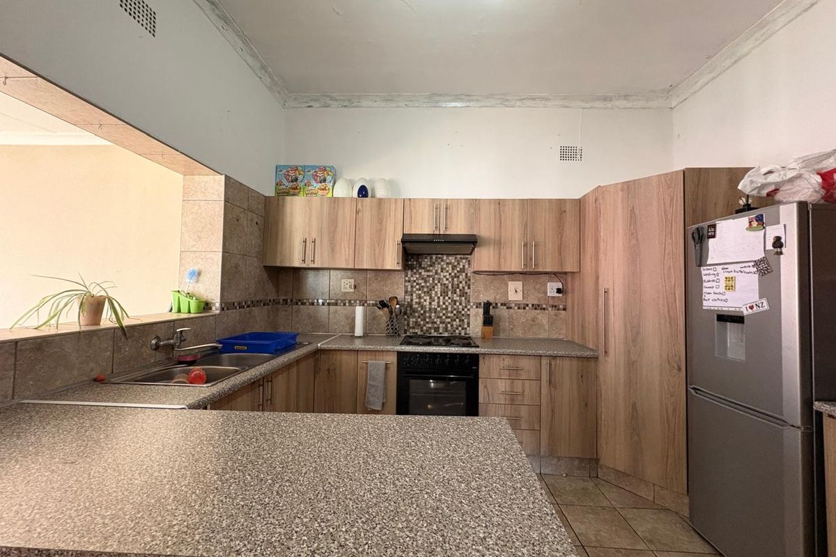 A functional kitchen featuring wood-look laminate cabinetry, granite-style countertops, a built-in oven with extractor fan, and a breakfast bar overlooking the living area.