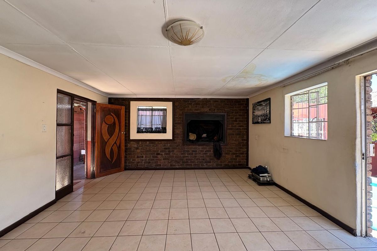 An empty living room featuring a brick fireplace, tiled flooring, and ceiling tiles, with visible signs of water damage on the ceiling.