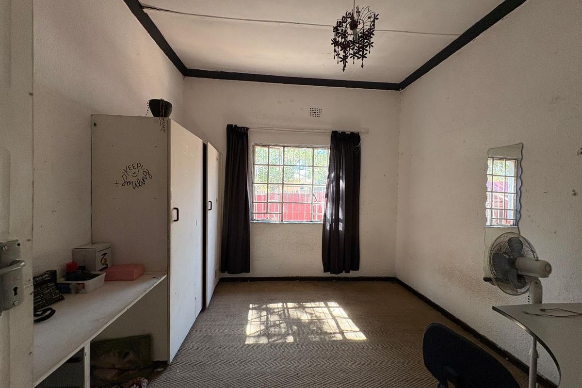 A bedroom featuring built-in cupboards, carpeted flooring, and security bars on the window, requiring cosmetic updates to improve its overall condition.