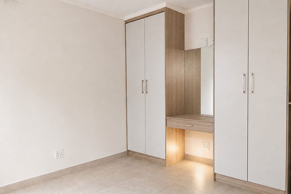 A clean, modern bedroom featuring neutral tiled flooring and extensive built-in cabinetry with an integrated vanity and lighting.