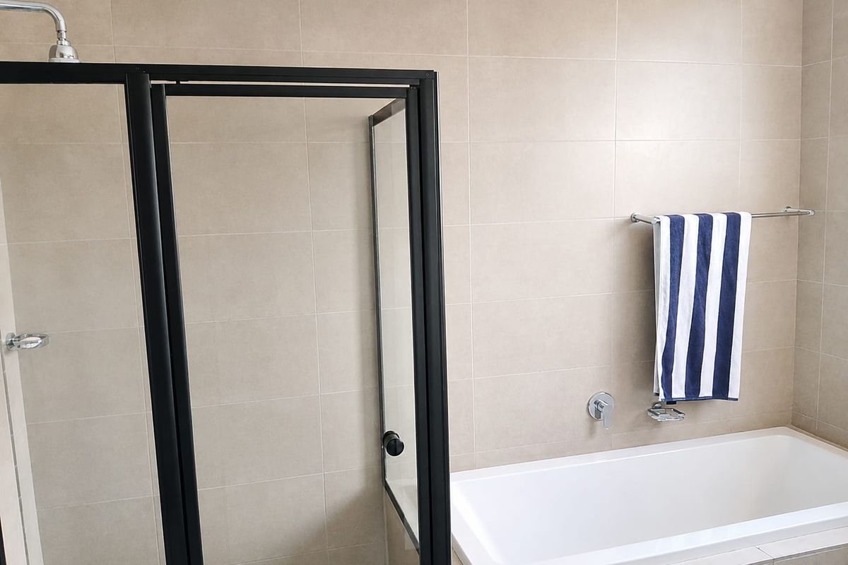 Modern bathroom featuring a built-in bathtub, a separate shower enclosure with black framing, and neutral ceramic wall tiling.