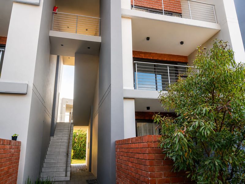 Modern apartment building exterior featuring a concrete staircase, brick accents, and balconies with stainless steel railings.
