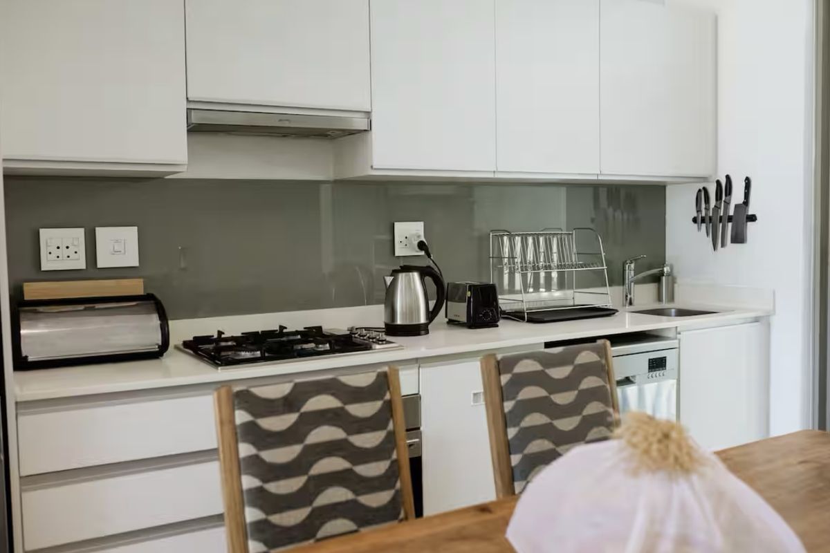 Modern kitchen featuring white cabinetry, a gas hob with extractor fan, integrated dishwasher, and a sleek glass splashback.
