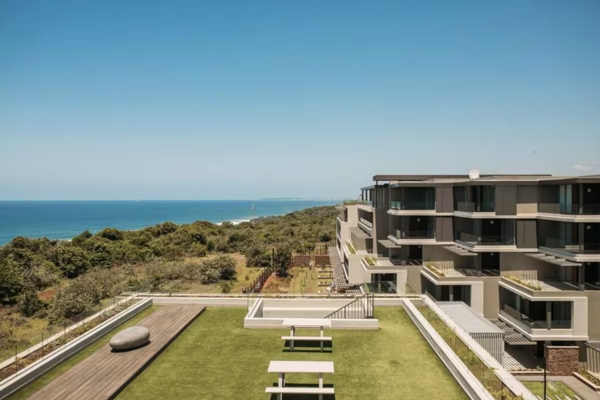 Aerial view of a modern apartment complex featuring landscaped rooftop gardens, timber decking, and expansive ocean views.
