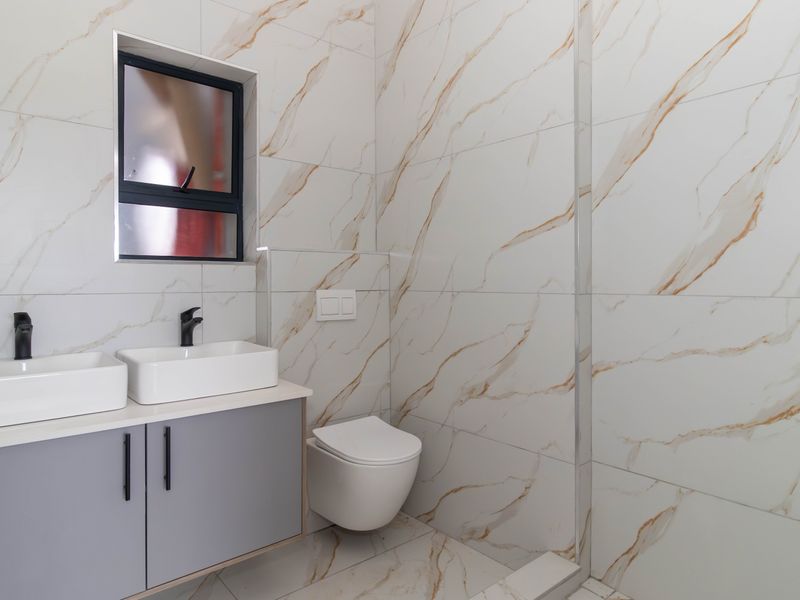 Modern bathroom featuring a double vanity with grey cabinetry, wall-mounted toilet, and elegant marble-effect tiling throughout with a walk-in shower.