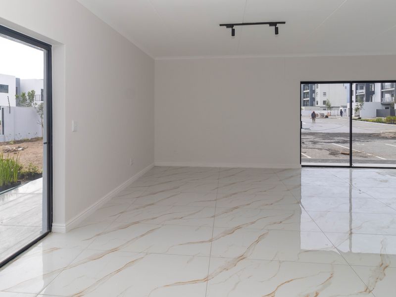 A bright, empty living area featuring modern marble-look porcelain floor tiles, black aluminium sliding doors, and contemporary track lighting.