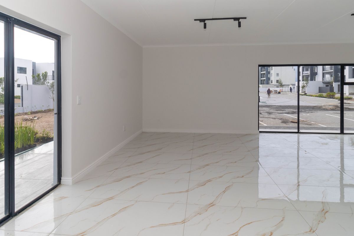 A bright, empty living area featuring modern marble-look porcelain floor tiles, black aluminium sliding doors, and contemporary track lighting.