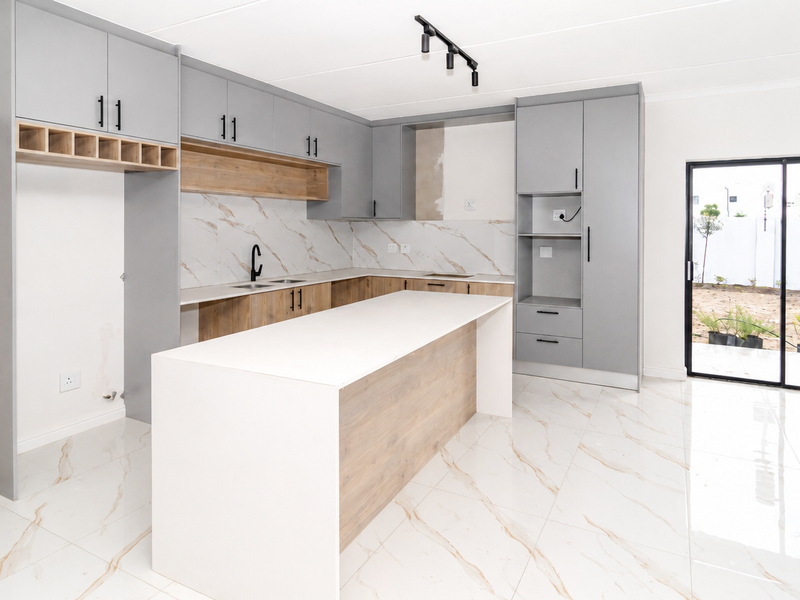 Modern open-plan kitchen featuring grey and wood-tone cabinetry, a central island, marble-look tiling, and direct access to the outdoor area through sliding glass doors.