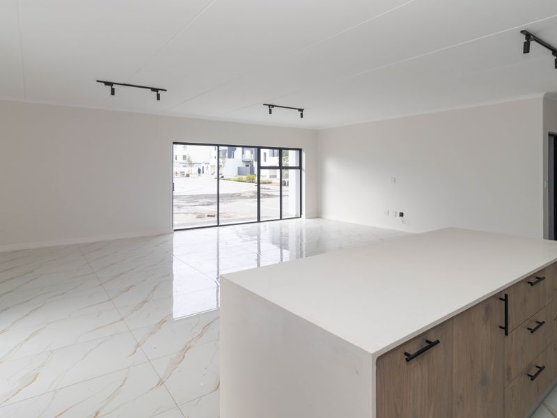 Modern open-plan living area featuring high-gloss marble-look floor tiles, a contemporary kitchen island with quartz countertops, and large sliding doors leading to the exterior.