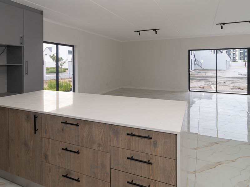 Modern open-plan living area featuring a kitchen island with quartz countertops, sleek cabinetry, and polished marble-look floor tiles with large sliding glass doors.