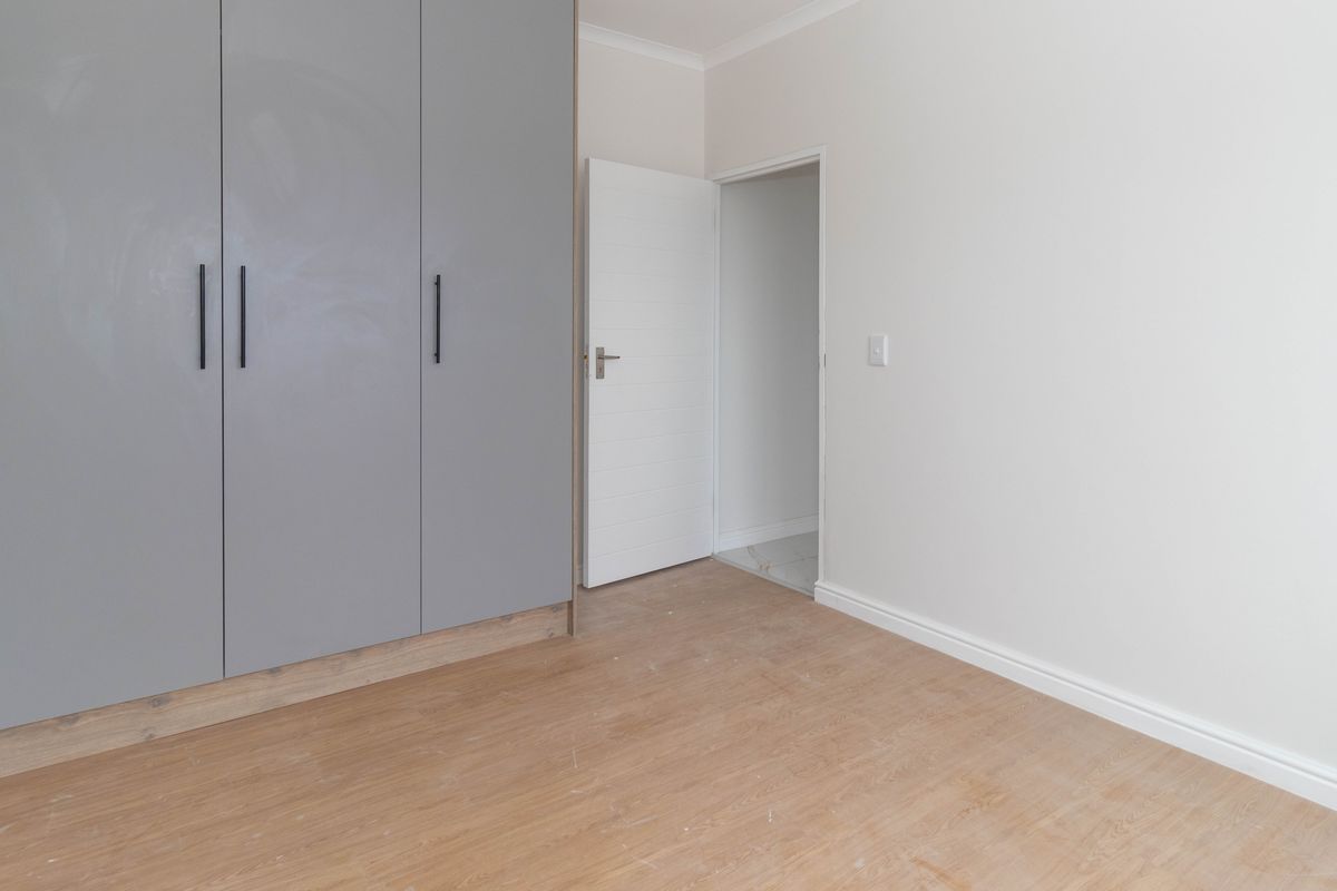 A clean, empty bedroom featuring modern grey built-in cupboards, light wood-look laminate flooring, and neutral wall finishes.