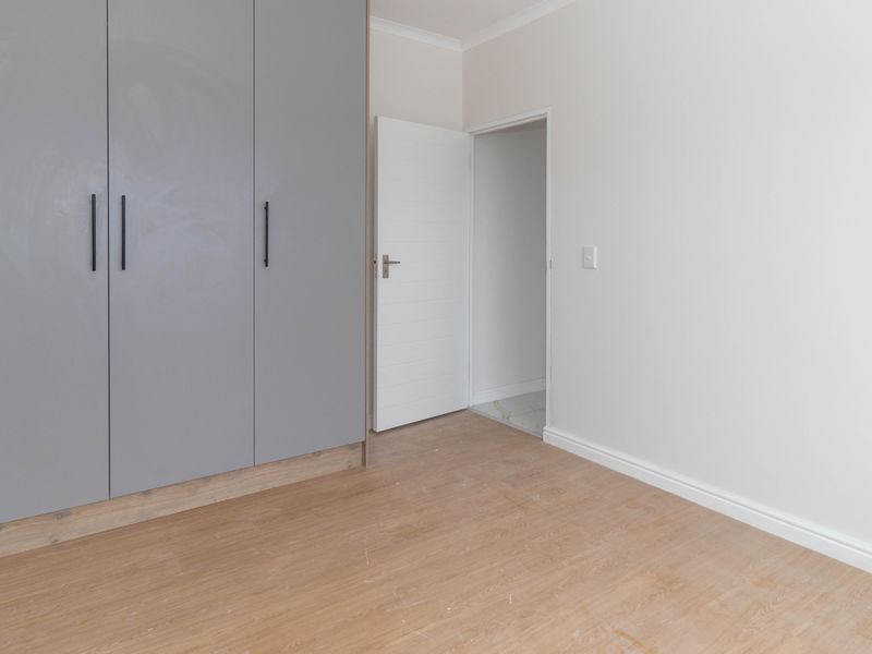 A clean, empty bedroom featuring modern grey built-in cupboards, light wood-look laminate flooring, and neutral wall finishes.