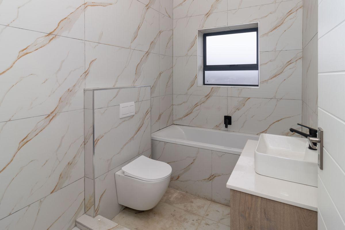 Modern bathroom featuring marble-look wall tiles, a wall-mounted toilet, a built-in bathtub, and a contemporary vanity with a vessel sink.