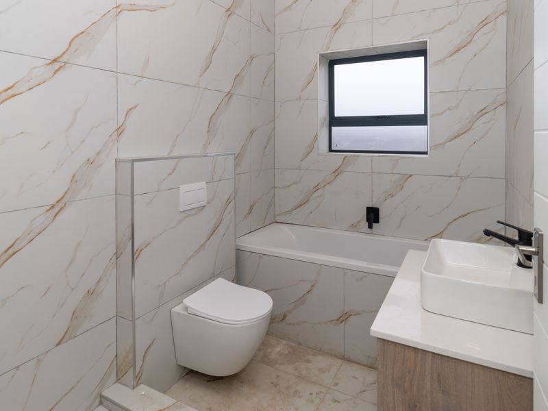 Modern bathroom featuring marble-look wall tiles, a wall-mounted toilet, a built-in bathtub, and a contemporary vanity with a vessel sink.