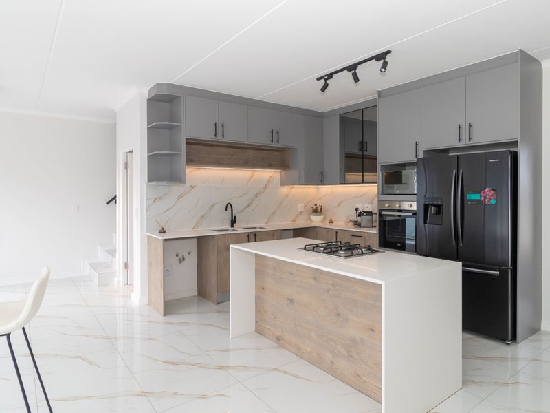 Modern open-plan kitchen featuring a central island with gas hob, sleek grey cabinetry, marble-look splashback, and high-quality porcelain floor tiles.