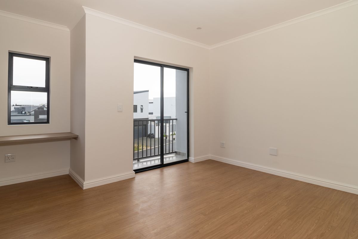 A bright, empty bedroom featuring laminate flooring, a built-in desk, and a sliding glass door leading to a private balcony.