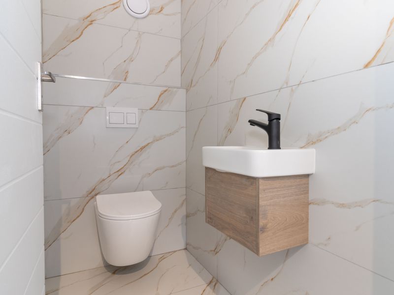 A modern, compact guest bathroom featuring high-end marble-look tiling, a wall-hung vanity with a black mixer tap, and a wall-hung toilet with a concealed cistern.