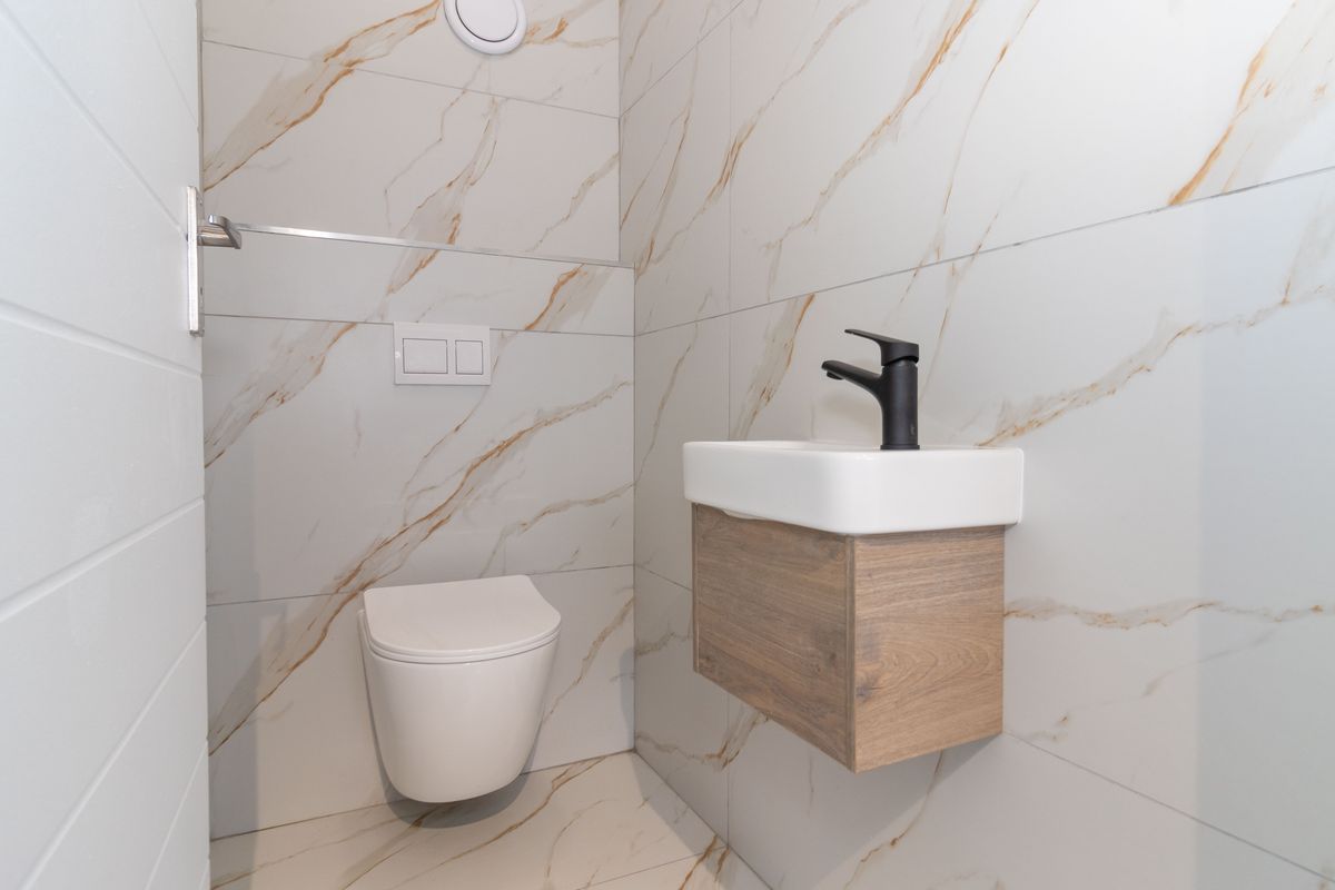 A modern, compact guest bathroom featuring high-end marble-look tiling, a wall-hung vanity with a black mixer tap, and a wall-hung toilet with a concealed cistern.