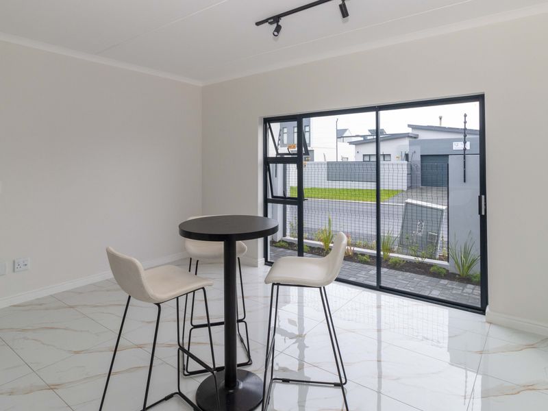 Bright and modern living area featuring high-gloss marble-look floor tiles, sleek black aluminium sliding doors, and contemporary track lighting.