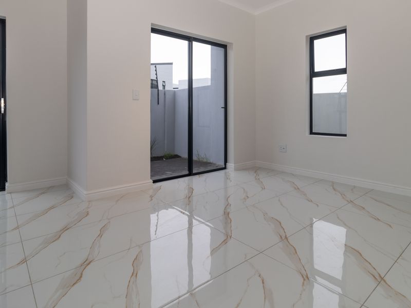Bright and modern living area featuring high-gloss marble-look floor tiles and direct access to an outdoor patio through black aluminium sliding doors.