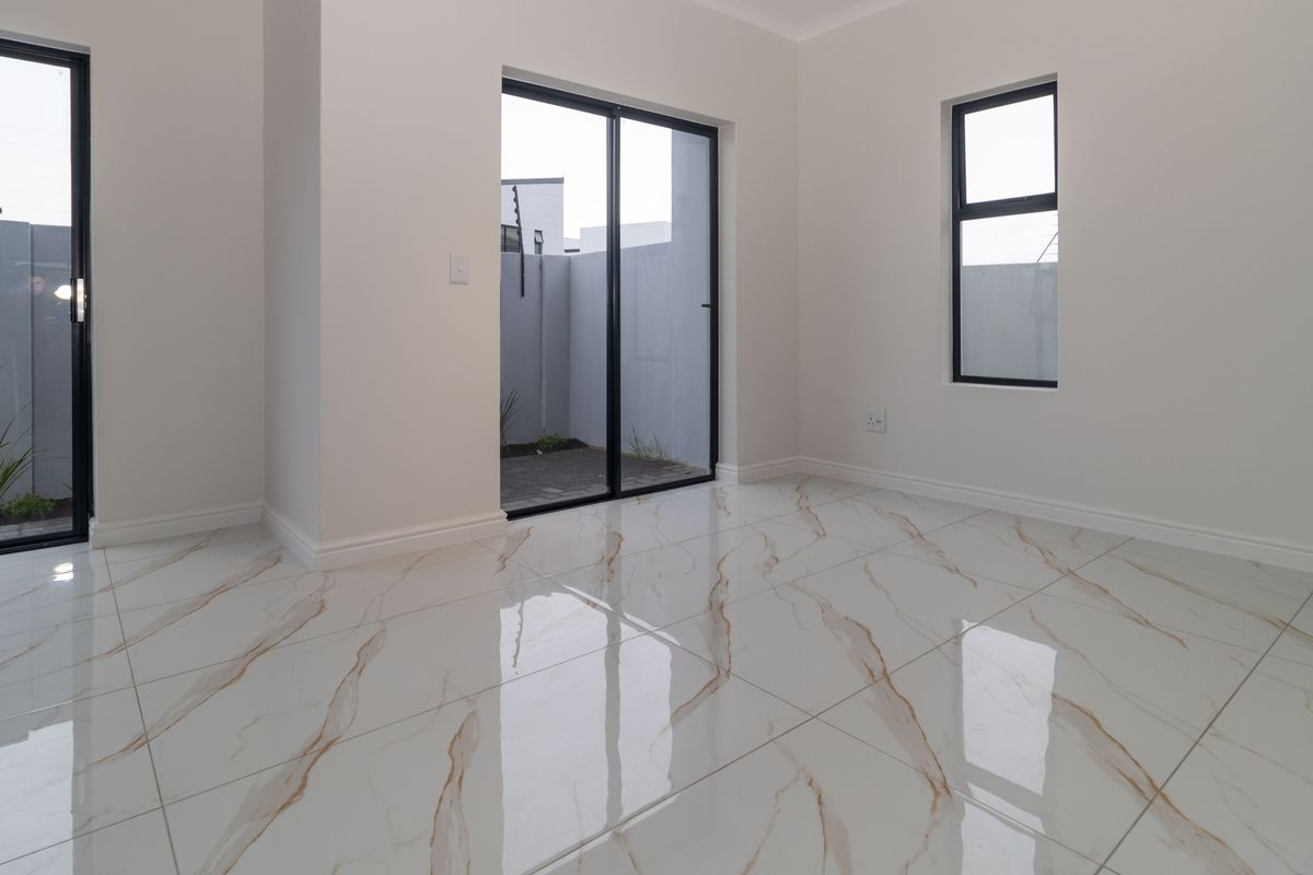 Bright and modern living area featuring high-gloss marble-look floor tiles and direct access to an outdoor patio through black aluminium sliding doors.