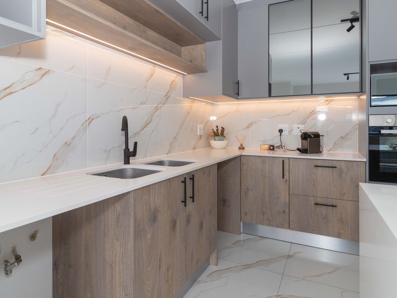 Modern kitchen featuring wood-grain cabinetry, quartz countertops, marble-look splashbacks, integrated appliances, and high-quality matte black fixtures.