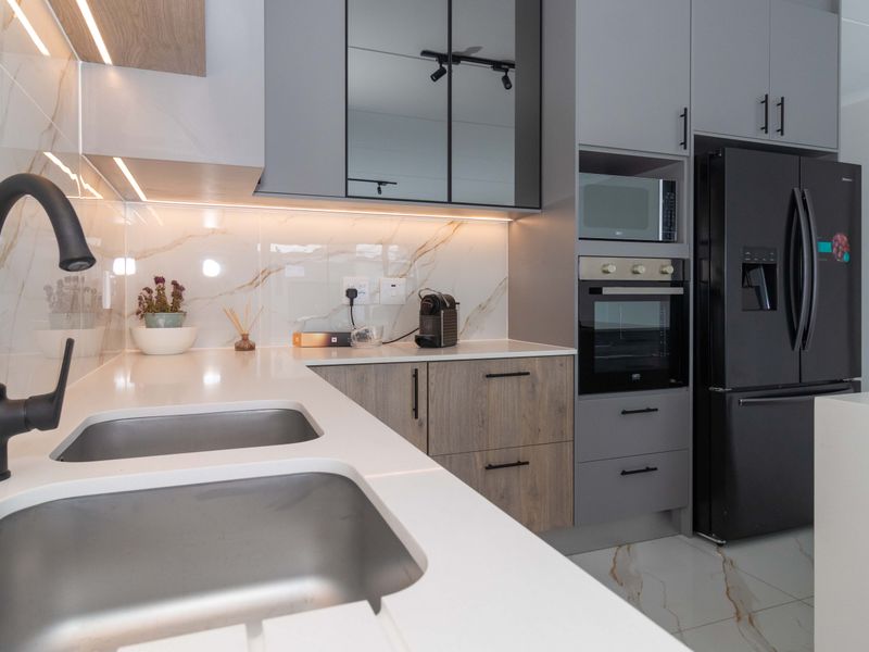 Modern kitchen featuring high-end finishes, including quartz countertops, marble-look splashback, integrated appliances, and sleek matte black fixtures.