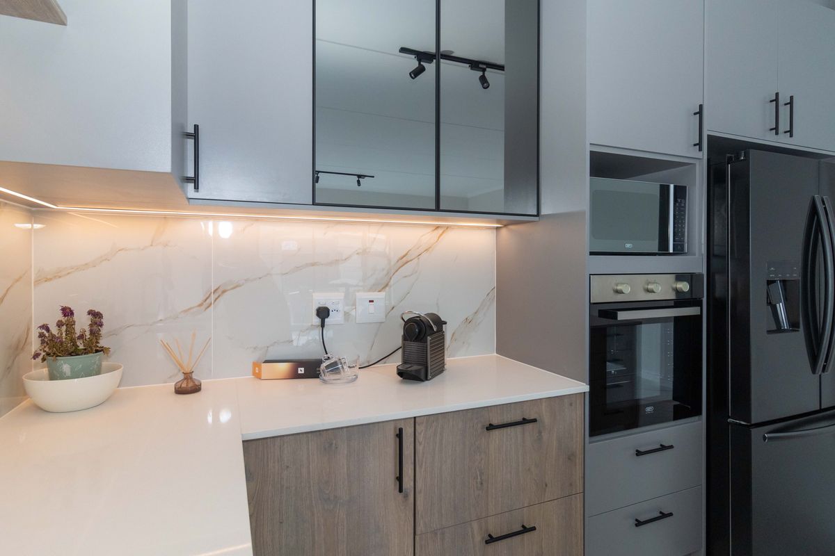 Modern kitchen featuring sleek grey and wood-tone cabinetry, marble-look splashback, integrated appliances, and high-quality quartz countertops with under-cabinet lighting.