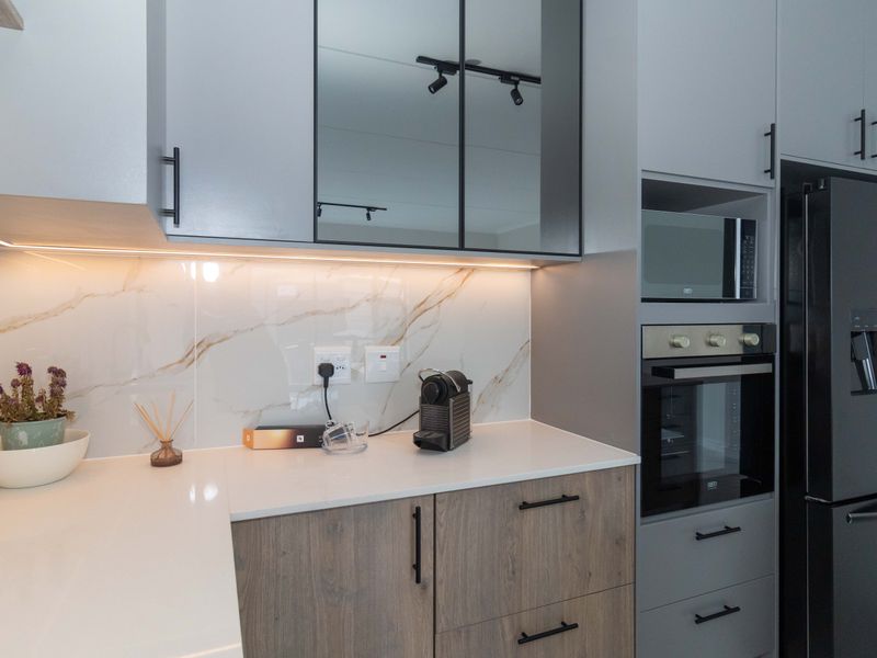 Modern kitchen featuring sleek grey and wood-tone cabinetry, marble-look splashback, integrated appliances, and high-quality quartz countertops with under-cabinet lighting.