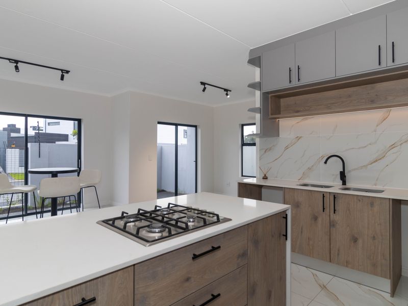 Modern open-plan kitchen featuring a central island with gas hob, sleek wood-finish cabinetry, marble-look splashback, and direct access to the outdoor patio area.