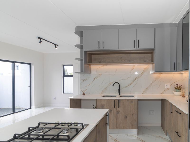 Modern open-plan kitchen featuring a central island with gas hob, marble-look finishes, integrated cabinetry, and sleek track lighting in a bright, contemporary space.