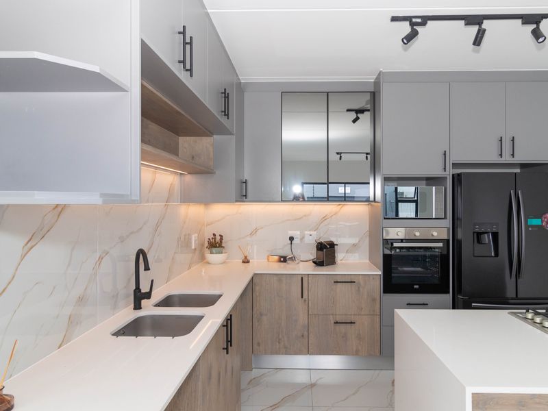 Modern kitchen featuring two-tone cabinetry, stone countertops, marble-look splashback, integrated appliances, and contemporary track lighting.