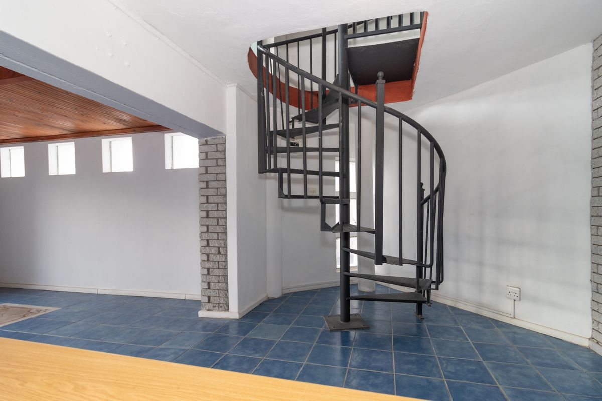 An open-plan living area featuring a prominent black metal spiral staircase, blue tiled flooring, and unique timber ceiling accents.