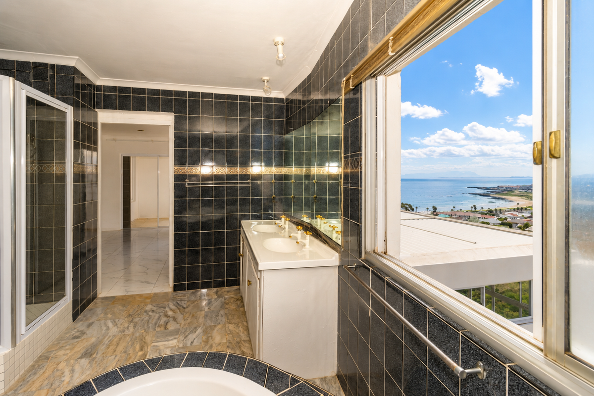 Spacious bathroom featuring a double vanity, shower, and built-in bathtub, complemented by expansive coastal views through a large window.