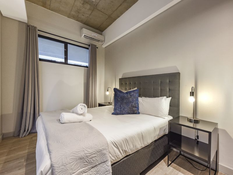 Modern bedroom featuring an exposed concrete ceiling, laminate flooring, and a wall-mounted split-system air conditioner.