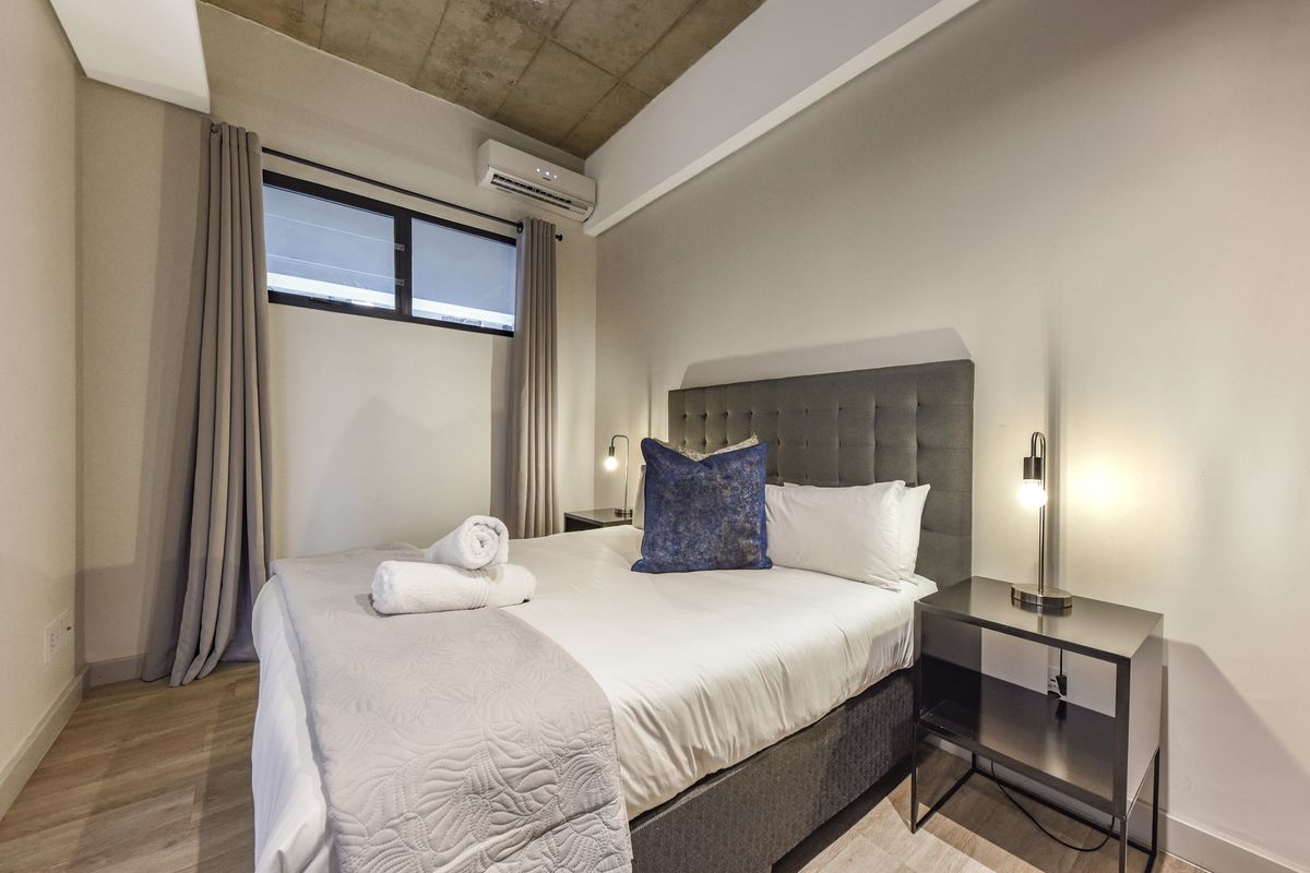 Modern bedroom featuring an exposed concrete ceiling, laminate flooring, and a wall-mounted split-system air conditioner.