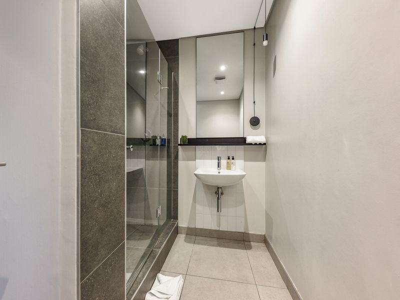 A modern, clean bathroom featuring a glass-enclosed shower, wall-mounted basin, and neutral tiled finishes.