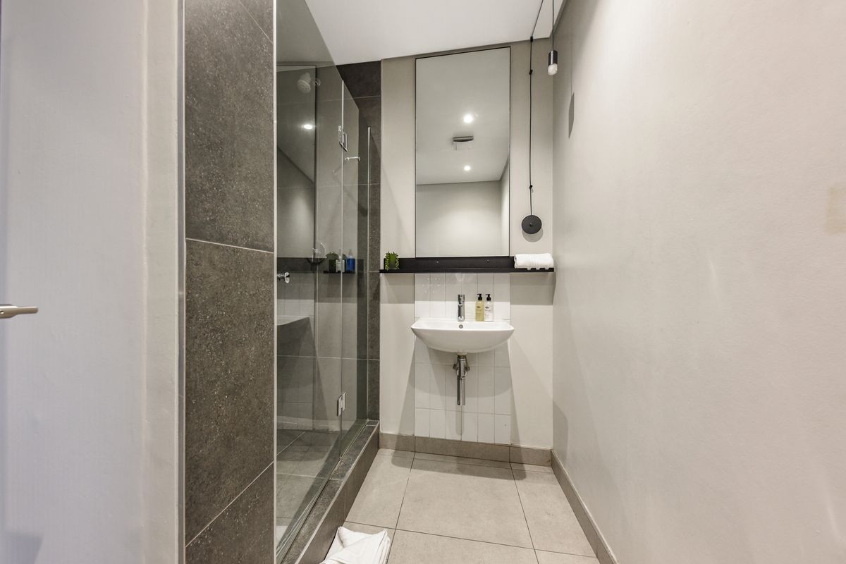 A modern, clean bathroom featuring a glass-enclosed shower, wall-mounted basin, and neutral tiled finishes.