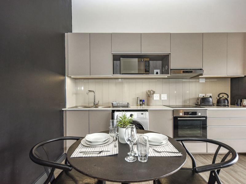 Modern kitchen featuring sleek cabinetry, integrated appliances including an oven, hob, and microwave, with a functional tiled backsplash and under-counter laundry space.