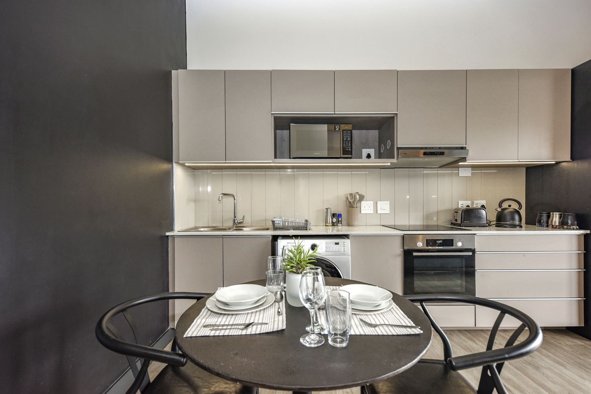 Modern kitchen featuring sleek cabinetry, integrated appliances including an oven, hob, and microwave, with a functional tiled backsplash and under-counter laundry space.