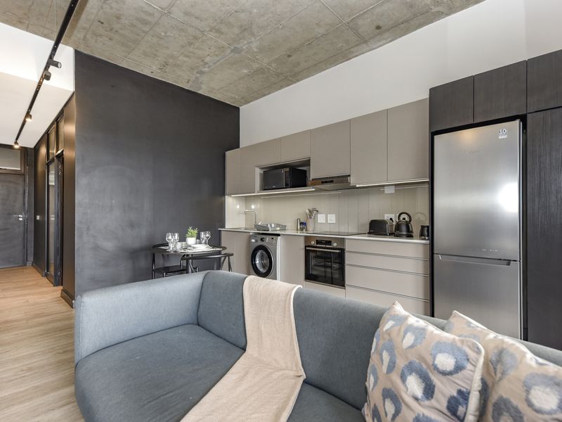 Modern open-plan apartment featuring an exposed concrete ceiling, sleek cabinetry, integrated kitchen appliances, and durable laminate flooring in a contemporary living space.