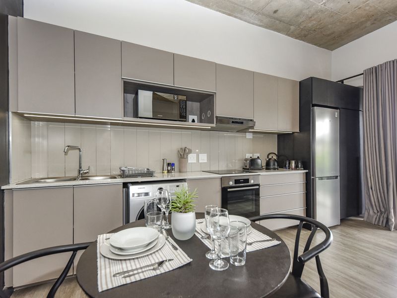 Modern open-plan kitchen featuring sleek cabinetry, stone countertops, integrated appliances, and an exposed concrete ceiling, seamlessly flowing into the living area.