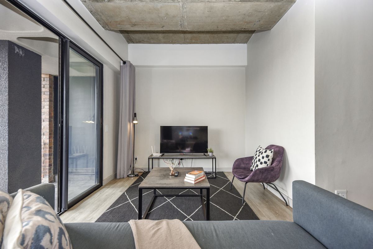 Modern living room featuring an exposed concrete ceiling, laminate flooring, and large sliding glass doors providing access to the outdoor area.