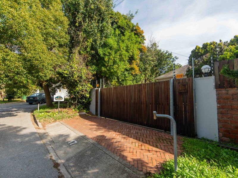 Front entrance view featuring a timber slat gate, brick boundary wall with electric fencing, and a herringbone brick driveway.